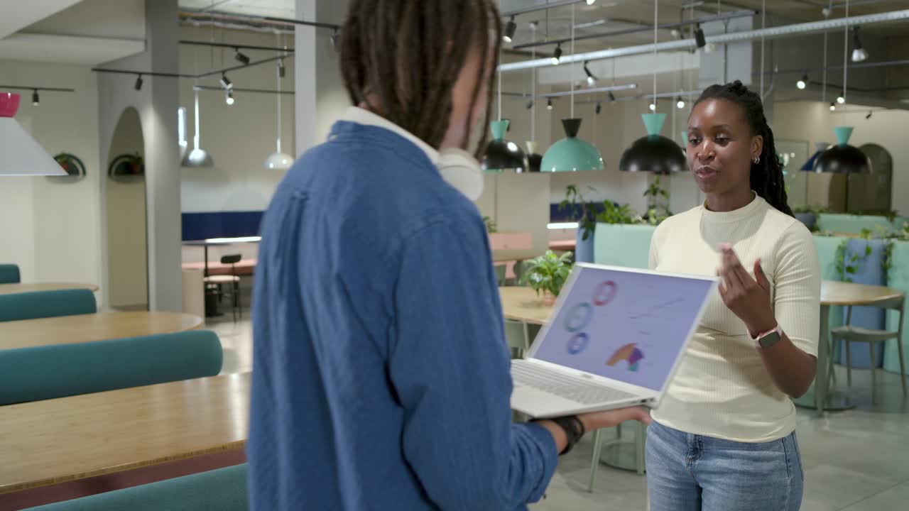 Afroamerikanske kolleger gennemgår laptop-diagrammer, efter at manden har vist skærmen på kontoret til et møde.