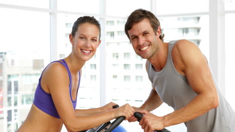 Fit-couple-exercising-on-bikes-in-fitness-studio