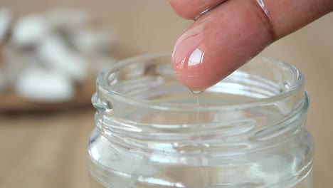 a close up of a finger dripping coconut oil into a glass jar