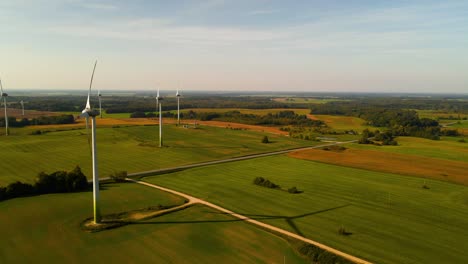 Drohnenaufnahme-Der-Windturbinen,-Die-In-Einem-Windpark-Arbeiten-Und-An-Einem-Sonnigen-Tag-Auf-Einer-Weiten-Grünen-Wiese-Grüne-Elektrische-Energie-Erzeugen,-Nutzung-Erneuerbarer-Energiequellen,-Folie-Nach-Links