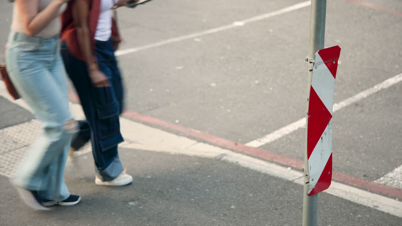 Persone di diverse etnie che entrano dal marciapiede, attraversano a sinistra oltre un palo a strisce rosse e bianche, mentre vanno al lavoro; spazio per il testo.