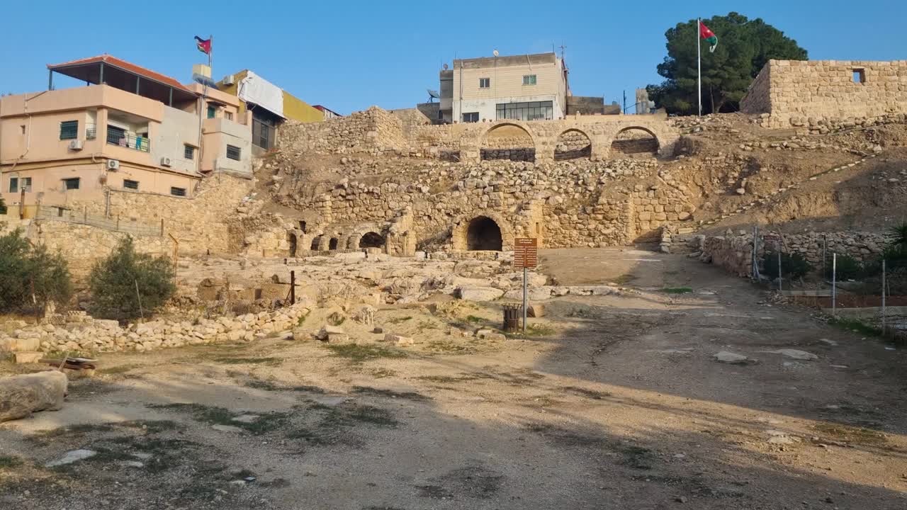 Scena di antiche rovine nel centro di Madaba, in Giordania, in una luminosa giornata di sole, con due bandiere giordane che sventolano nella brezza sotto un cielo blu e un cane randagio nelle vicinanze