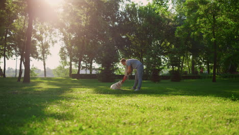 Owner-teasing-golden-retriever-in-sunny-park.-Dog-holding-toy-in-teeth-lying.