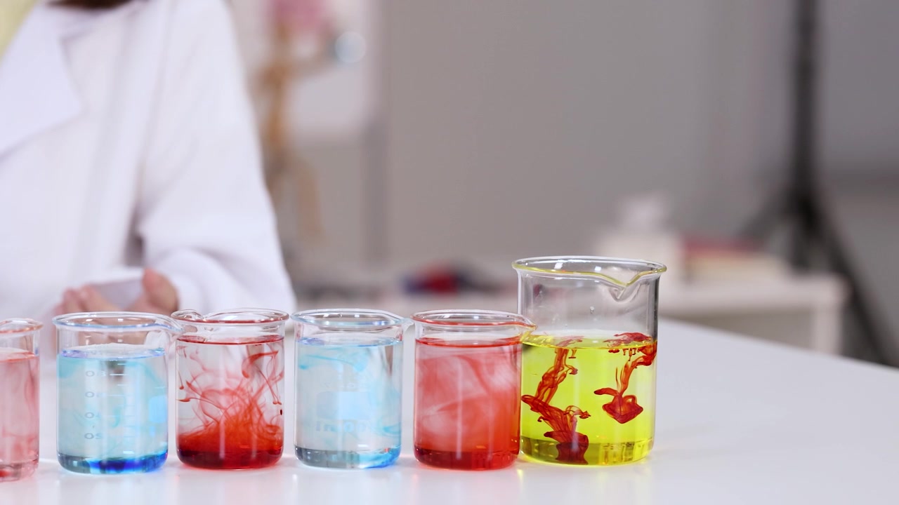 Nærbillede af studerende, der blander levende farvestoffer i glasbægerglas under en STEM-kemilektion i klasseværelset
