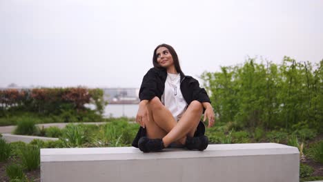 Cute-caucasian-model-sitting-down-on-modern-stone-bench-in-meditation-position-then-start-posing-touching-her-body-looking-around-showing-face-expressions-perfect-for-music-videos-cloudy-slow-motion