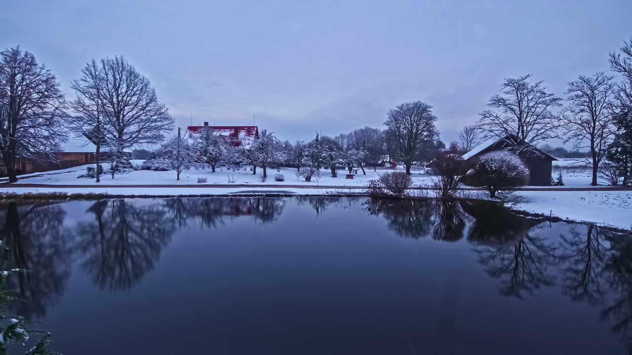 집과 나무가 있는 눈 덮인 얼음 풍경 속에서 호수의 시간 경과, 구름이 전진하고 있습니다.
