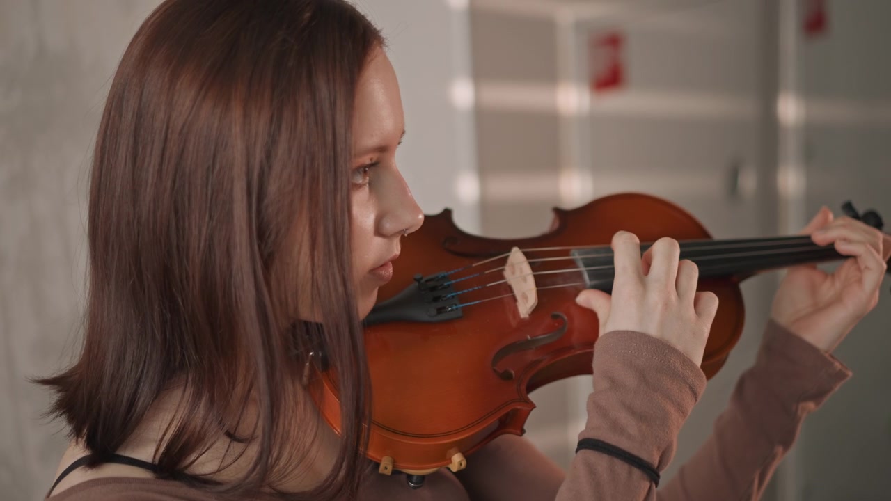 Youth plays violin. Young girl prepares instrument attentively. Teenage girl finetunes violin before practicing carefully. Female teenager adjusts her violin in quiet preparation for lesson