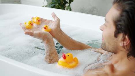 man relaxing in a bathtub with rubber ducks