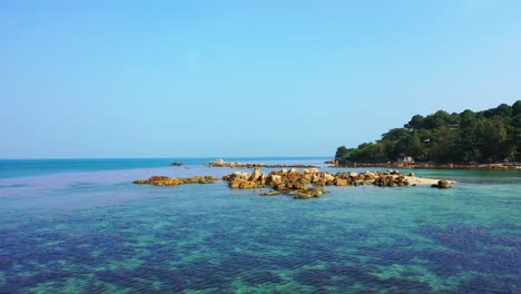 Cliffs-surrounded-by-calm-clear-water-of-shallow-lagoon-with-corals-and-pebbles-near-rocky-shore-of-tropical-island