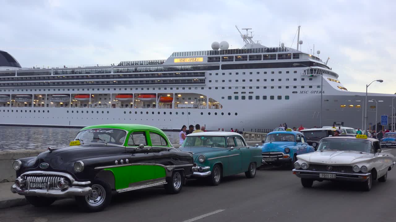 거대한 유람선이 전경에 고전적인 오래된 자동차가 있는 쿠바 하바나 항구에 정박합니다.