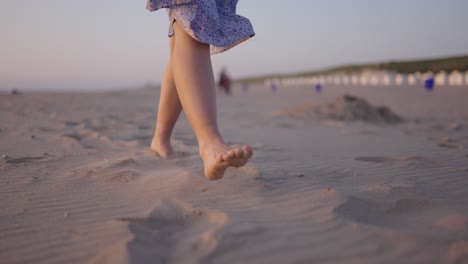 Caucasian-woman-walks-barefoot-on-beach-sand,-flowing-dress