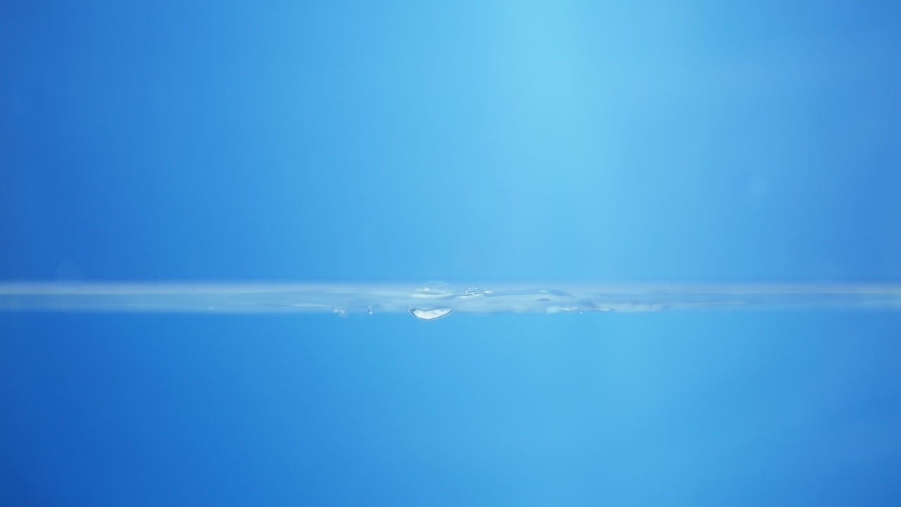 파란색 배경에 물로 가득 찬 용기에 작은 물방울과 파동을 일으키는 물 어리