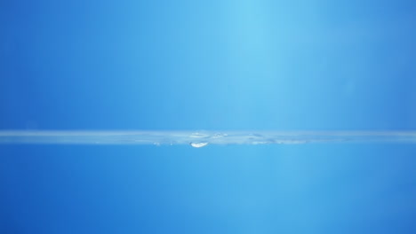 splattering water creating tiny droplets and ripples in a container filled with water against a blue background