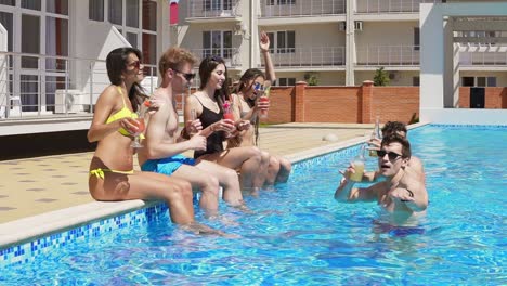 happy group of young friends hanging out with coctails and chatting at the side of the pool in the summertime 3