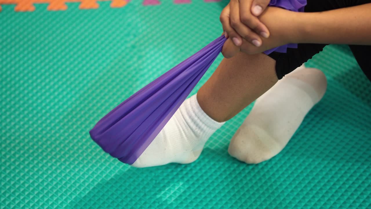 Close-up of foot moving with a purple elastic band during rehabilitation on a green mat.