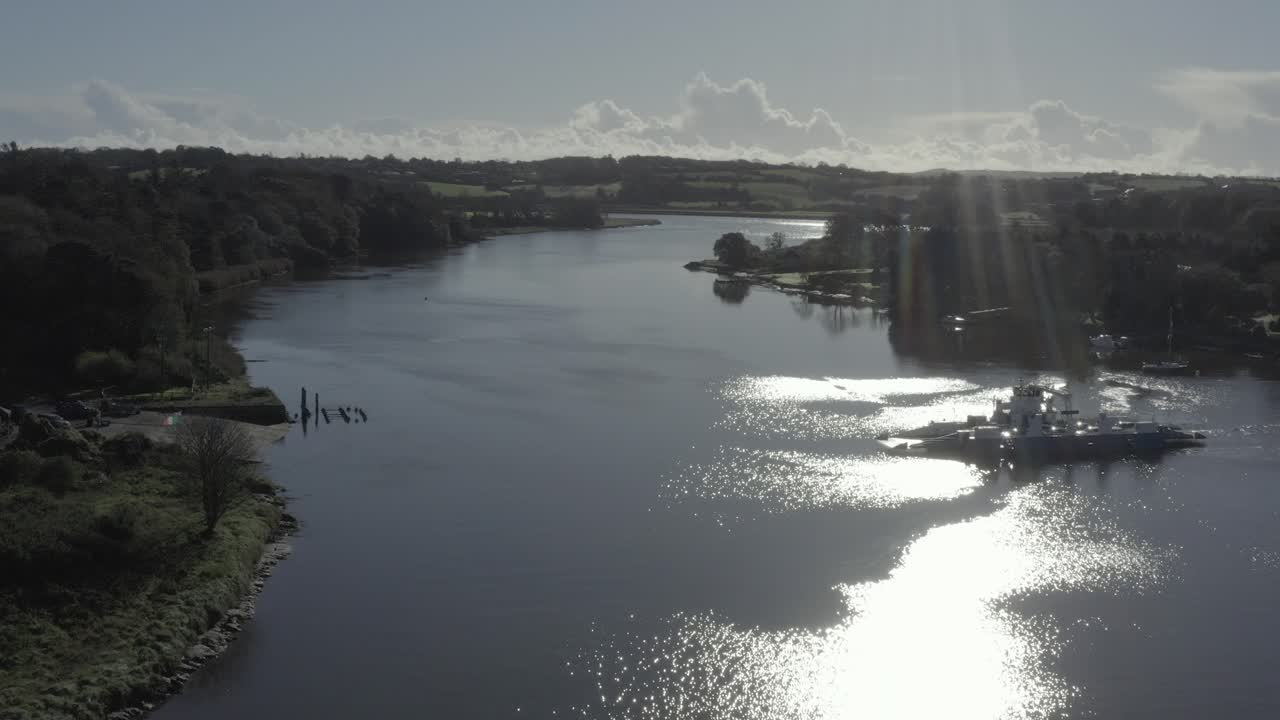 Small vehicle ferry crosses river with spectral sun beam, lens flare