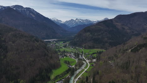 aerial view of scenic austrian alps landscape, green valley village and snow capped peaks on sunny spring day