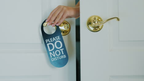 a female hand quickly hangs a do not disturb sign on a door hand