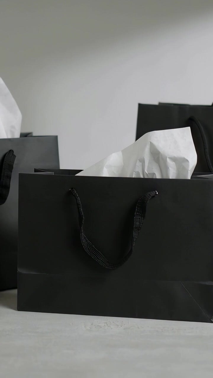 Vertical video: Shifting camera revealing black paper bag displaying tissue on tabletop for display