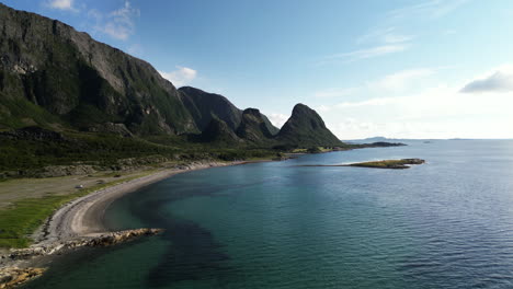 aerial drone shot of the coastline of the island of tomma, one of the nesna islands, norway. turquoise waters and cliff side can be seen either side of the shoreline and beach.