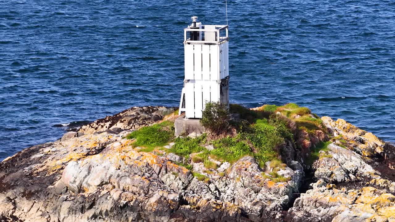 Drone circles small white lighthouse on rocky island, bright daylight, North Sea, steady movement