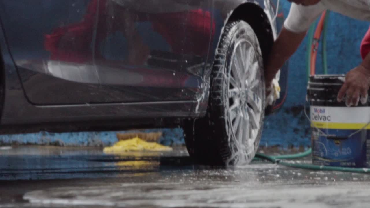 Barefoot worker cleaning car with soap in slow motion