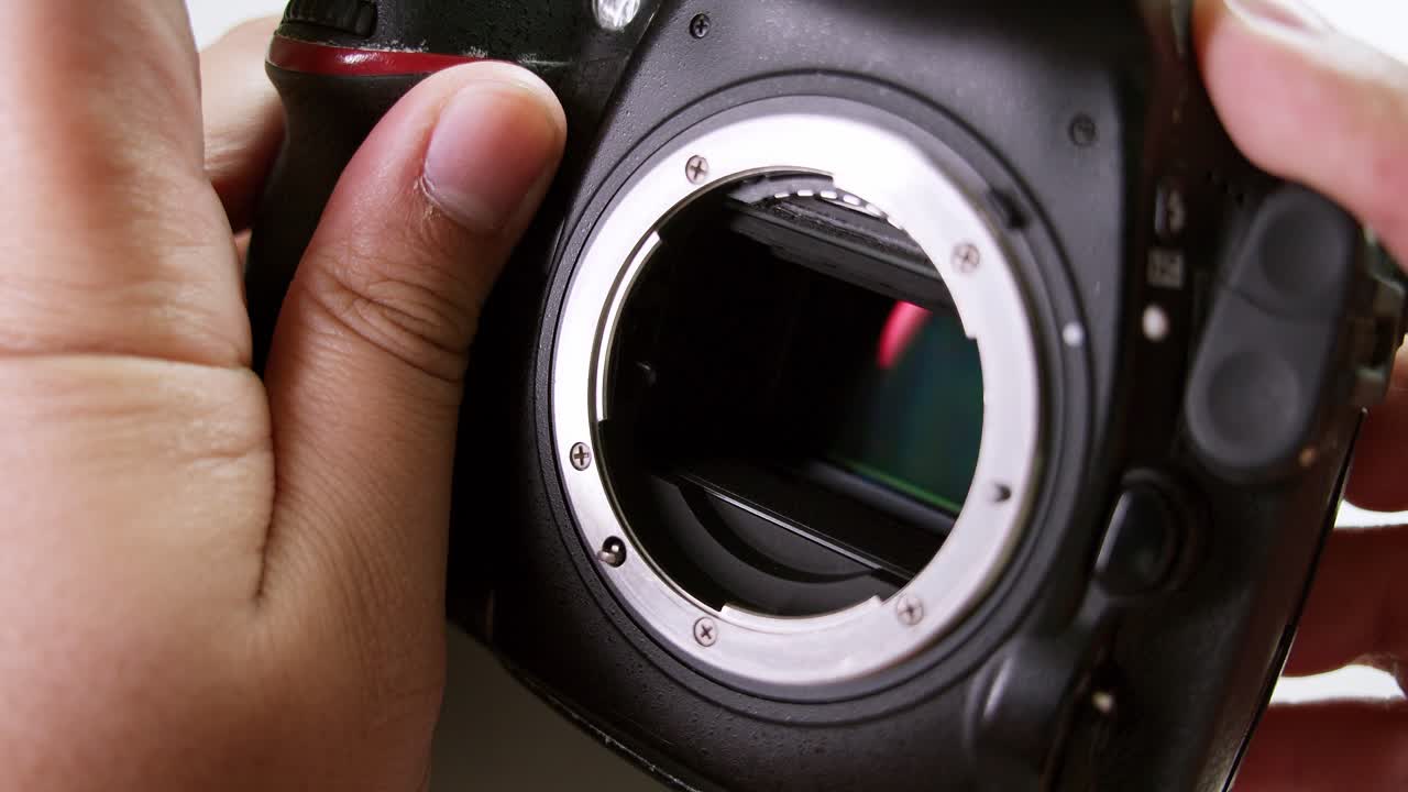 Lähikuva teknikosta laukaisemassa suljinta ja tarkistamassa huolellisesti DSLR-kameran kennoa.