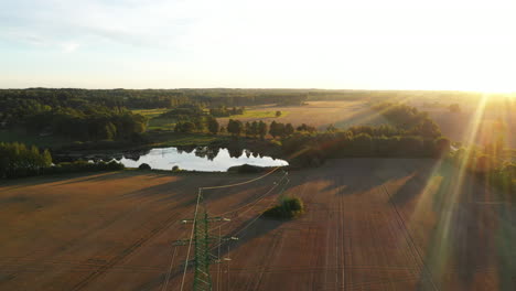 High-voltage-power-lines-on-agricultural-field,-energy-supply-to-rural-villages,-aerial-view-on-golden-hour