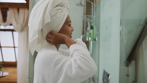 Mixed-race-woman-wearing-bathrobe-looking-at-mirror