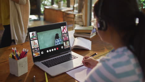 schoolgirl using laptop for online lesson at home, with diverse teacher and class on screen