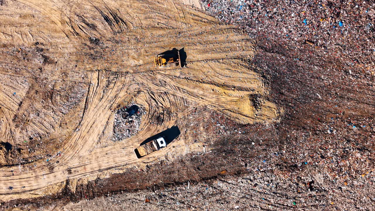 Aerial top view of bulldozer and truck at landfill. Drone shot of heavy machinery working on a waste management site with tire tracks on dirt ground