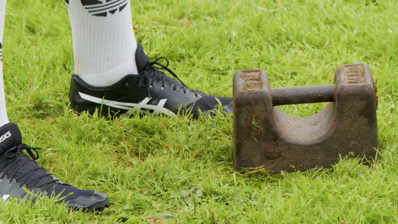Male athlete in sportswear lifts heavy stone during Highland Games on grassy field, Scotland