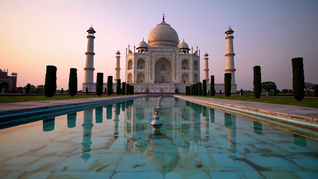A low-angle video captures the Taj Mahal at sunrise, reflecting in the serene pool
