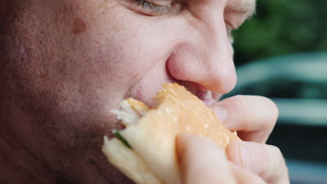 A-Hungry-Man-Eagerly-Eats-A-Hamburger-Only-His-Mouth-Is-Visible-In-The-Frame