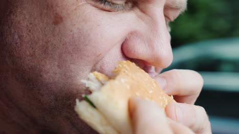 un hombre hambriento come ansiosamente una hamburguesa solo su boca es visible en el marco