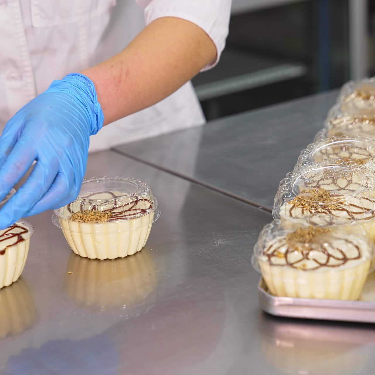 Sweet creamy desserts packaging. Worker's hands in latex gloves put the lids on individual plastic boxes of cake. Close up