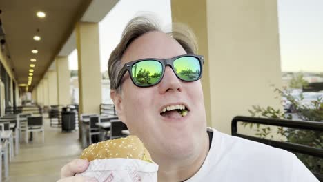 un hombre con gafas de sol disfruta de una hamburguesa.