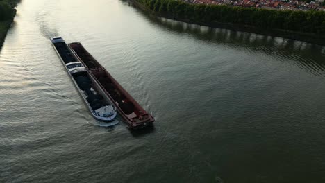 aerial - two cargo barges in a river in the netherlands, wide reverse shot