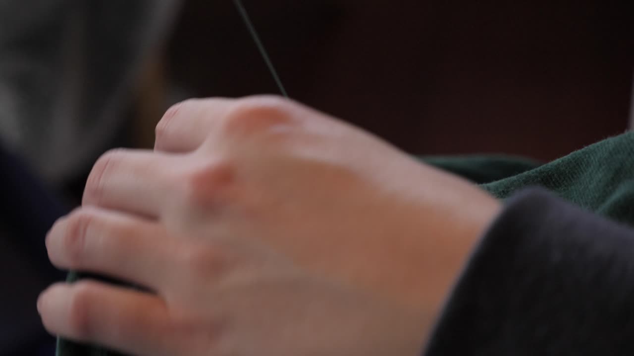 las manos femeninas cosen a mano el material de la chaqueta verde con una fina aguja de metal y un hilo de cuerda para hacer modificaciones y ajustes de sastrería, perspectiva lateral macro vista de primer plano tirando del hilo a través