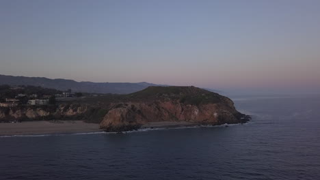 AERIAL:-flight-over-Malibu,-California-view-of-beach-Shore-Line-Pacific-ocean-at-sunset-with-mountain-cliff