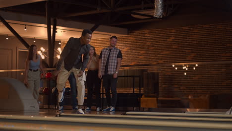 A-black-African-American-man-throws-a-bowling-ball-and-knocks-out-a-shoot-with-one-throw-and-hugs-and-rejoices-with-friends.-Multi-ethnic-group-of-friends-bowling