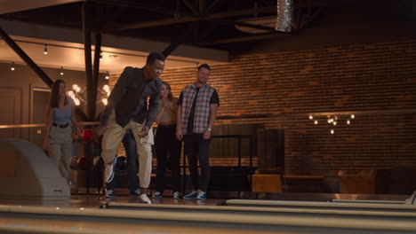 a black african-american man throws a bowling ball and knocks out a shoot with one throw and hugs and rejoices with friends. multi-ethnic group of friends bowling