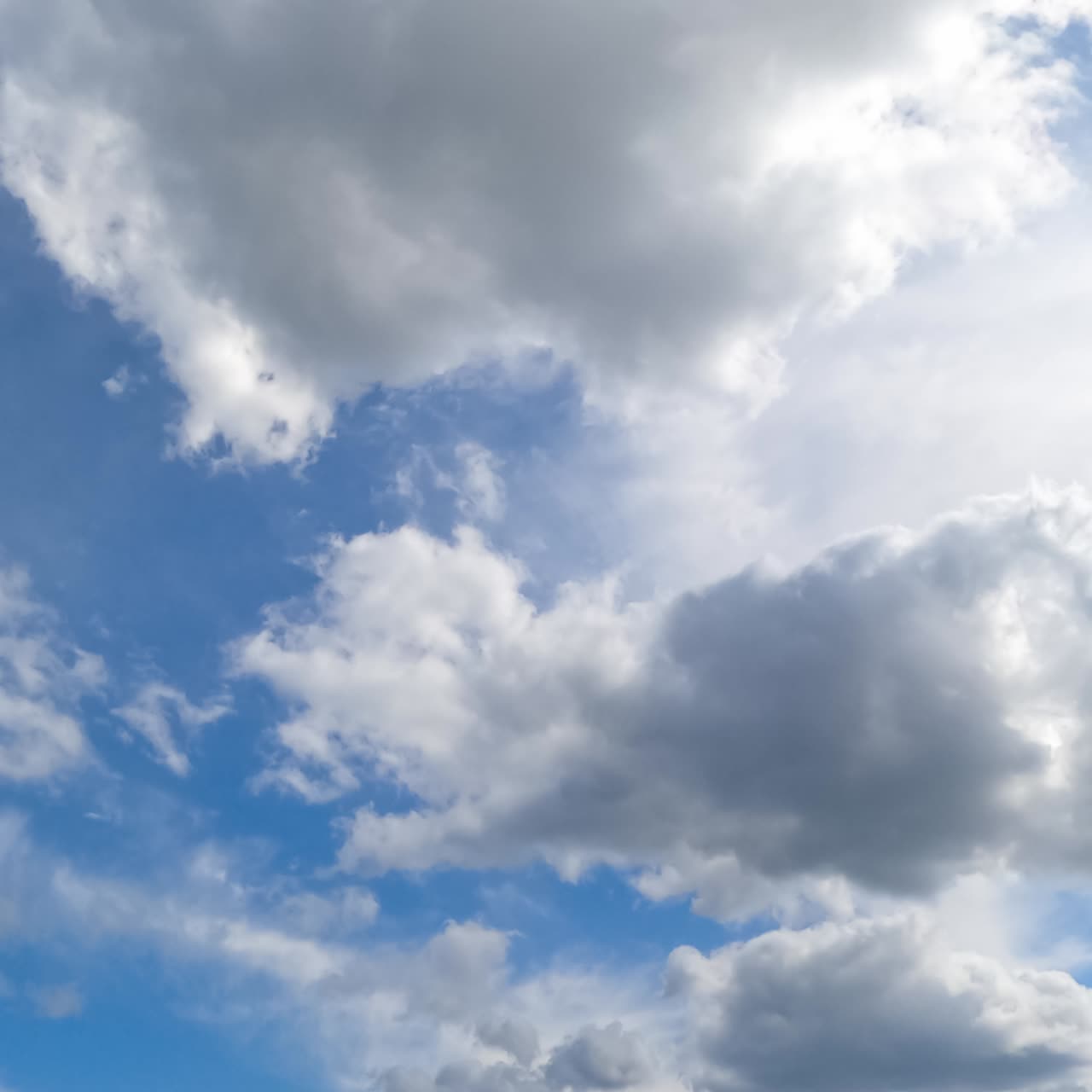 Cumulus and spindrift clouds transformation in the summer sky. Low angle view on the blue skies with multiple clouds. Timelapse