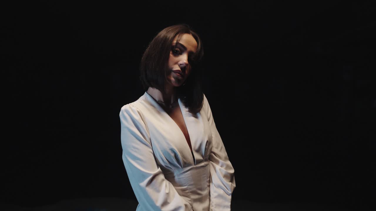woman posing in a white outfit. she stands sideways. black background slow motion