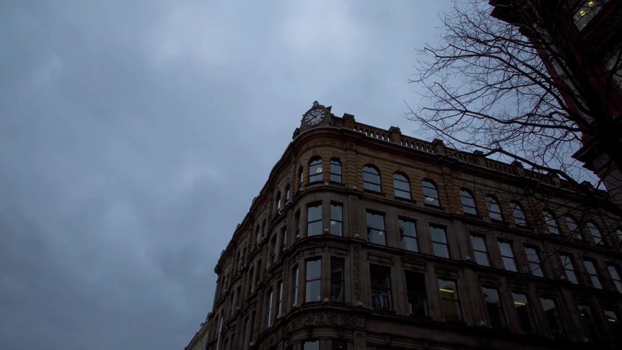 Timelapse suggestivo con zoom all'indietro da un grande orologio storico sull'angolo di un edificio della città di Belfast sotto nuvole temporalesche scure nell'Irlanda del Nord.