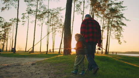 grandpa and grandson are walking together in forest or natural park in sunset time going to fishing on river shore