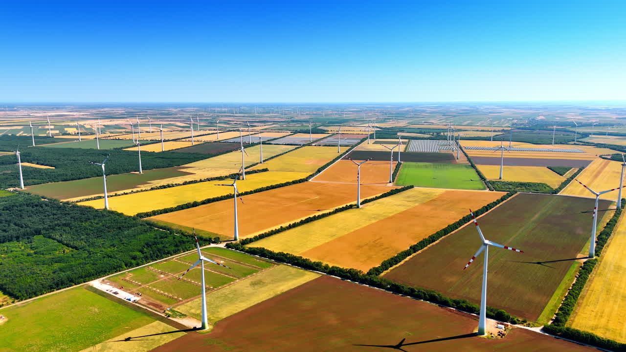 Vast sunny agricultural fields with wind turbines rotating in the wind. Alternative sources of energy, green energy concept. Aerial view