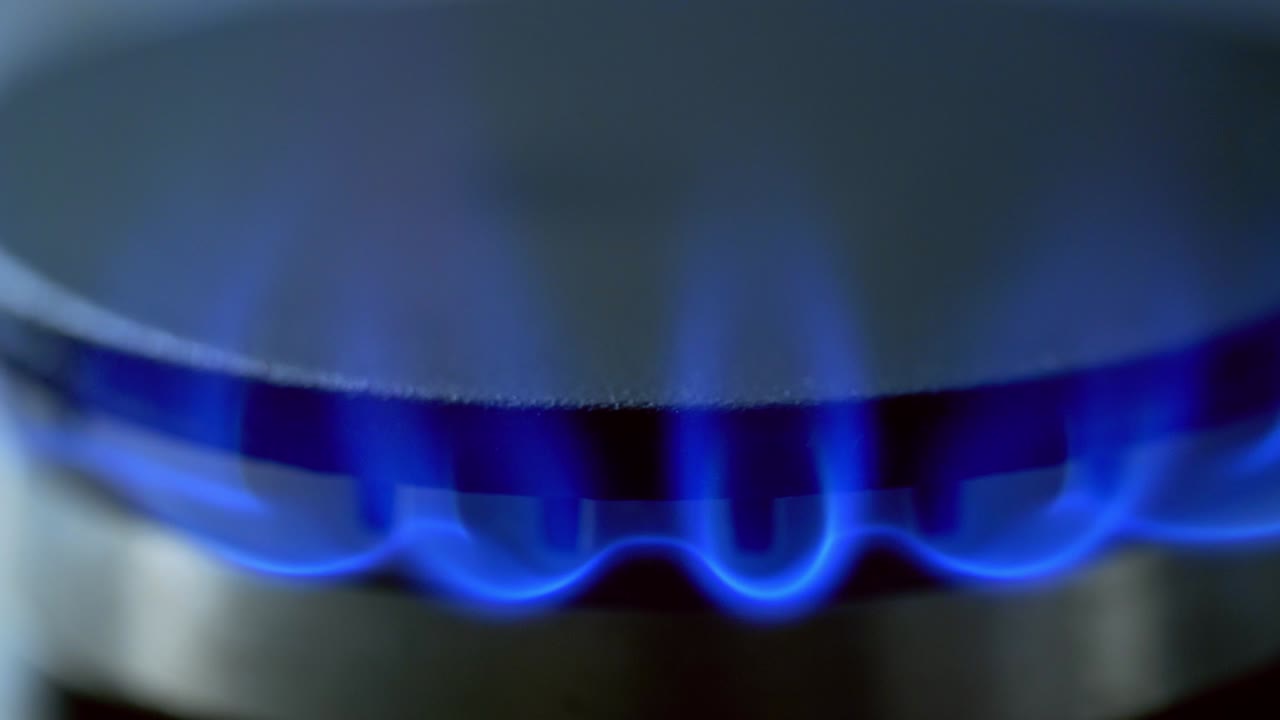 Gas is switching on automatically. Blue flame appearing on a gas stove on dark background. Close-up.