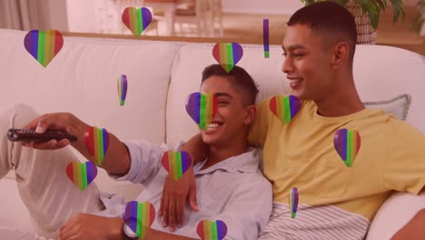 Animation-of-rainbow-hearts-over-male-couple-in-love-watching-television