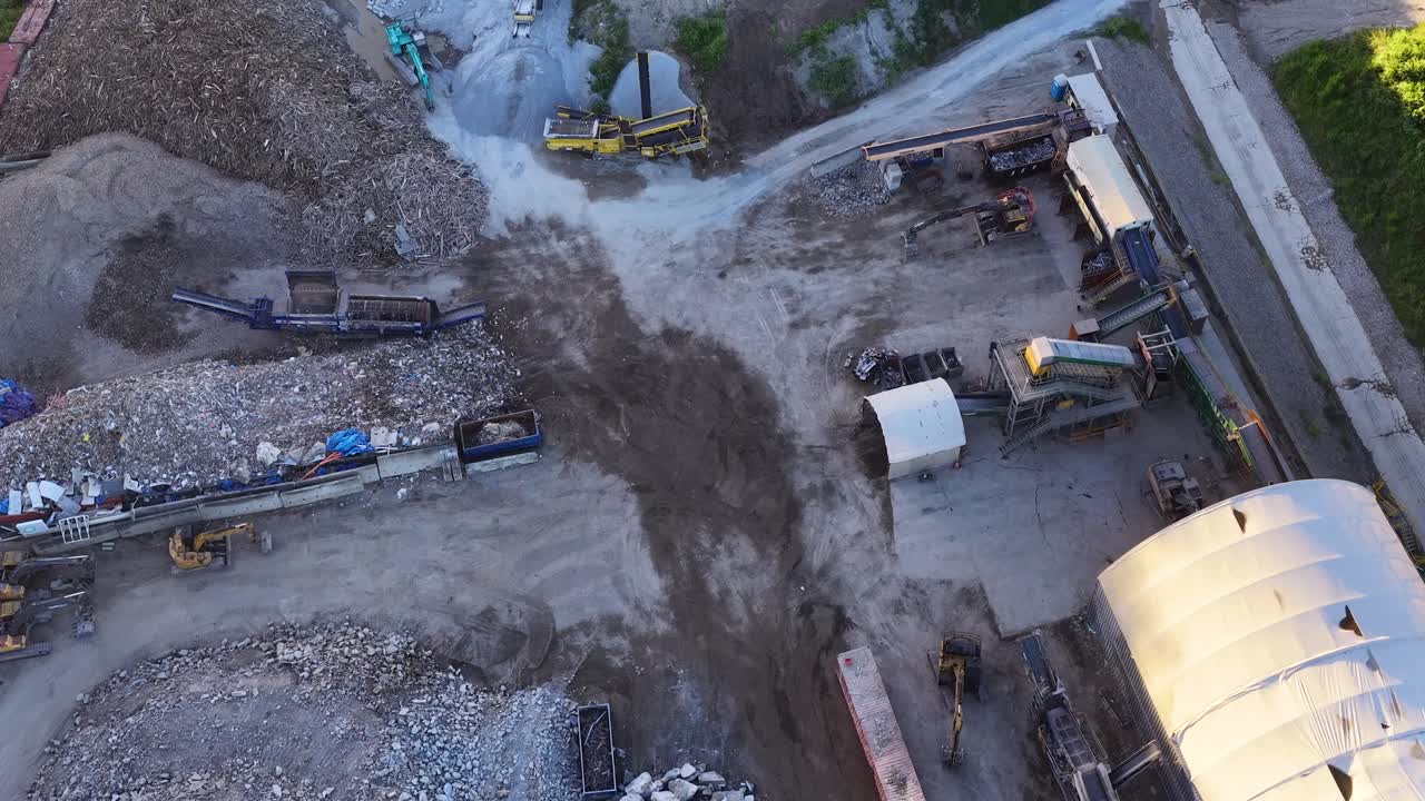 Inquadratura dall'alto con drone cattura macchinari pesanti che spostano detriti in un grande impianto industriale di riciclaggio